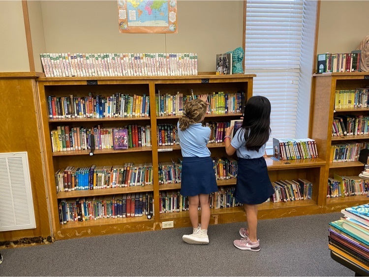 two 5th grade students standing in the immaculate heart of Mary library, picking out books to read for the school year  