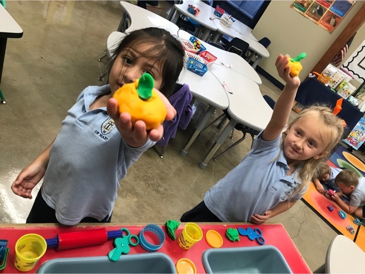 two students holding up play dough orange pumpkins with green stems