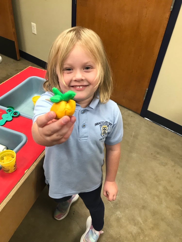 student holding play dough orange pumpkin with green stem 