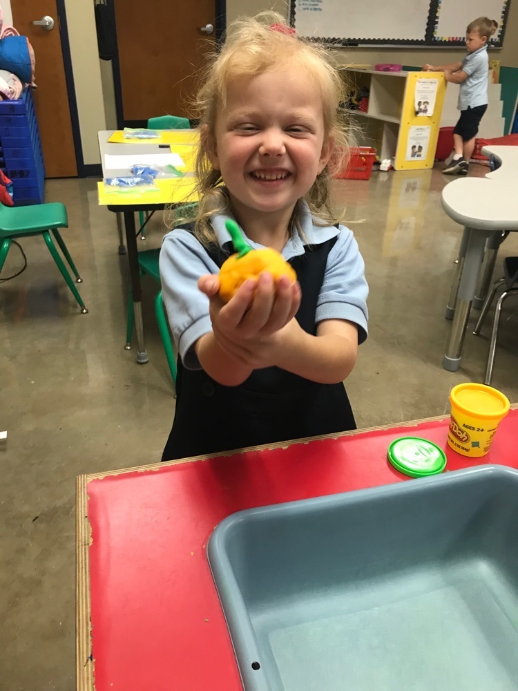 student holding up play dough orange pumpkin with green play dough stem 